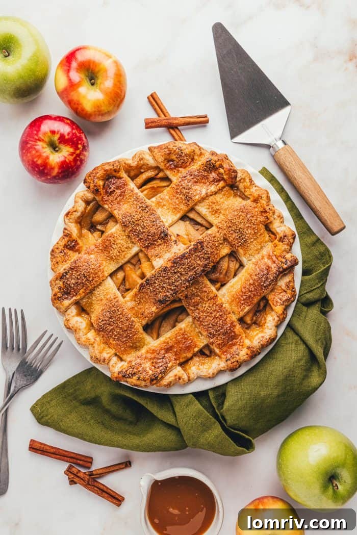 A warm, inviting caramel apple pie with a flaky cheddar crust, served in a rustic pie dish on a green linen napkin.