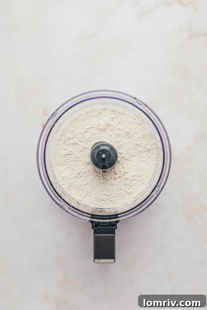 A food processor bowl containing a dry mixture of flour, sugar, and salt, ready for the next step in pie crust preparation.