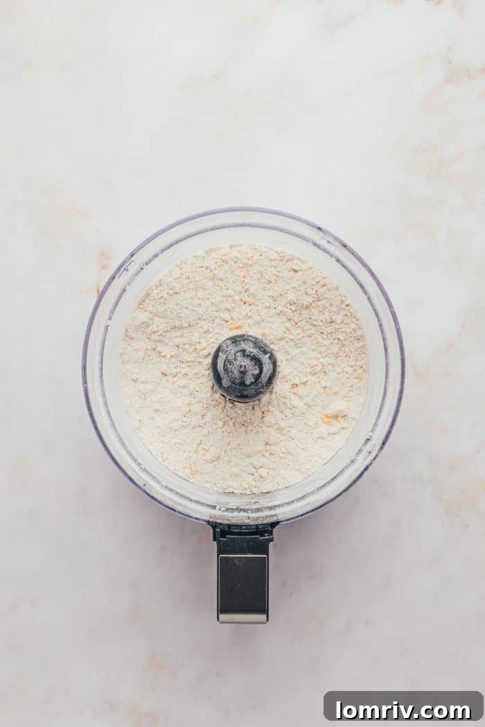 A food processor containing flour, sugar, salt, and cubes of cold butter, ready for pulsing to create a pie dough base.