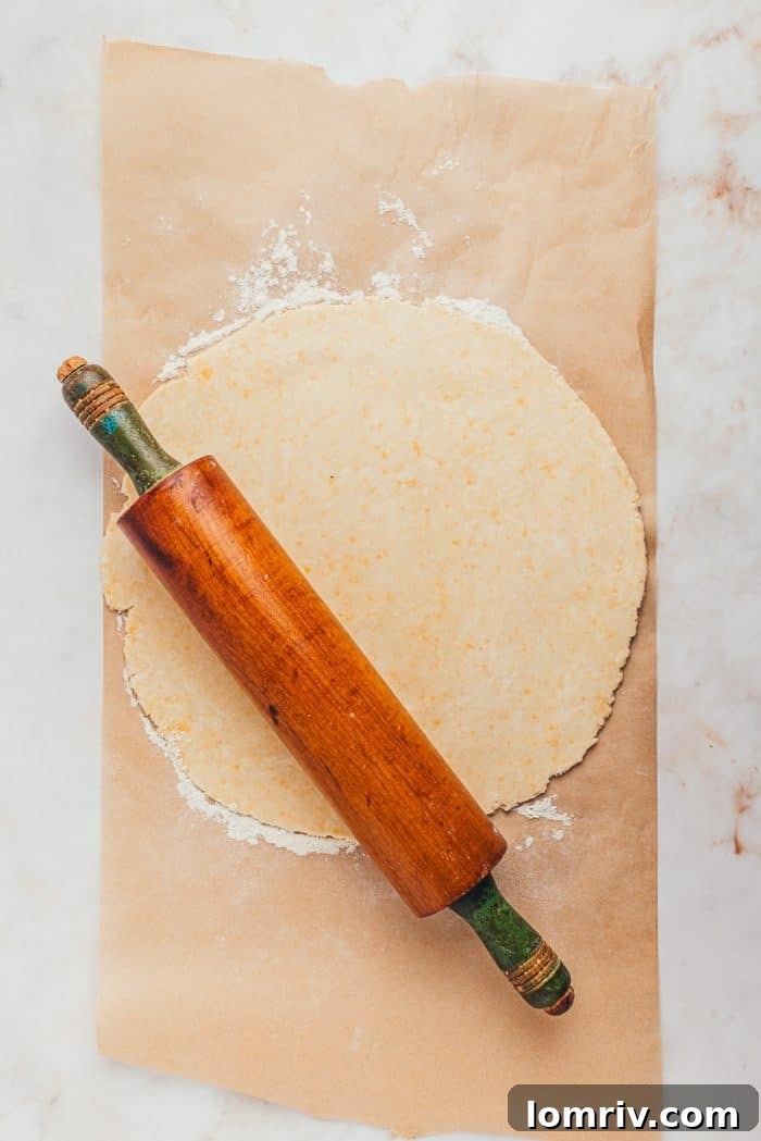A circular pie dough, expertly rolled out with a wooden rolling pin, lies on a floured surface, ready for placement in the pie dish.
