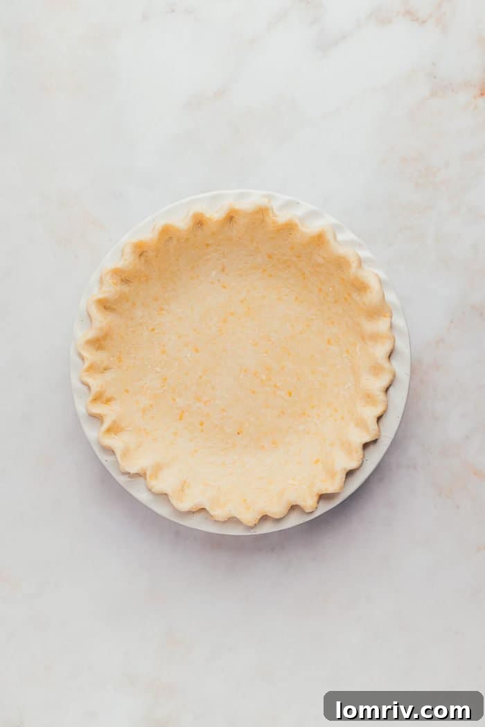 A pristine, unbaked pie crust expertly fitted into a white pie plate, with its edges beautifully crimped and ready for filling.