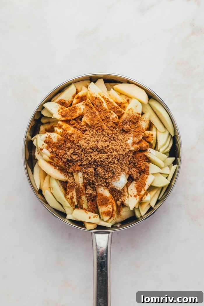 Sliced apples are generously sprinkled with cinnamon and sugar in a skillet, beginning the process of creating a sweet and spiced filling.