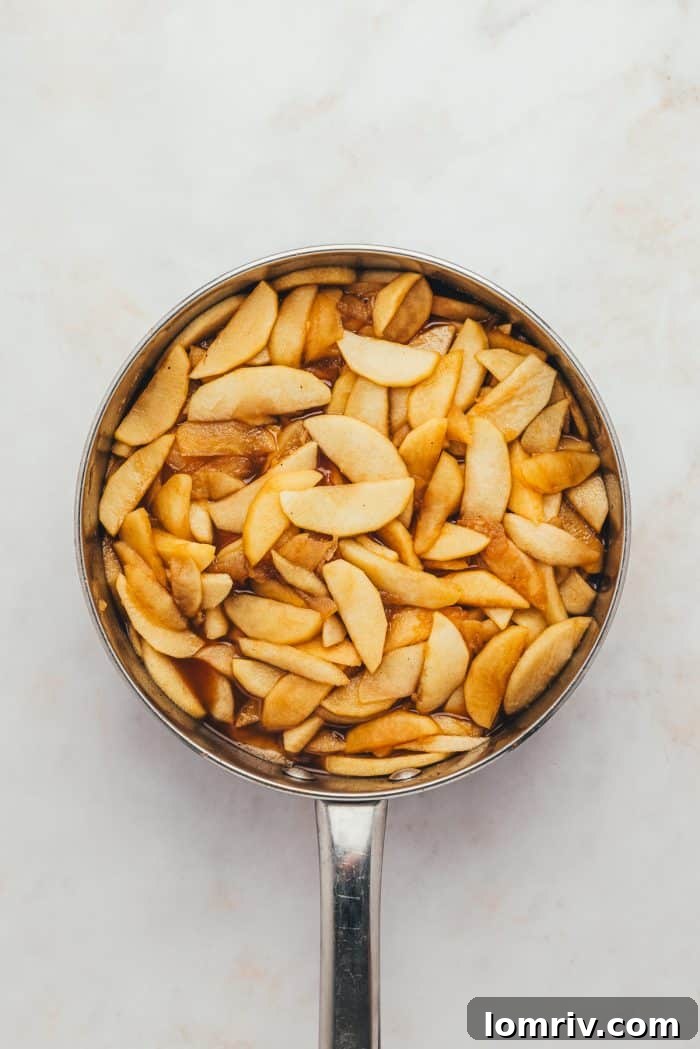 Sliced apples, now tender and glistening, are shown cooking gently in a skillet, transforming into the perfect pie filling.