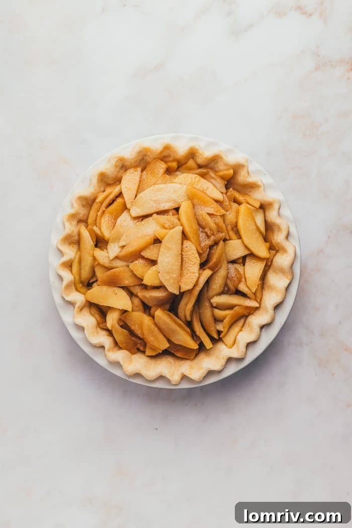 An unbaked pie filled with a generous mound of raw apple pie filling, showcasing its abundant and fresh ingredients.