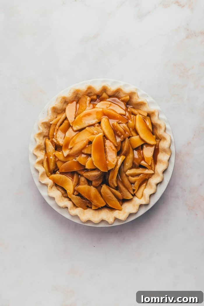 An unbaked pie with its raw apple filling now beautifully topped with a glistening drizzle of rich caramel sauce.