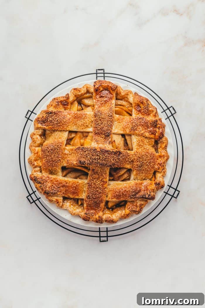 A freshly baked apple pie with a perfectly golden lattice crust rests on a wire cooling rack, emitting a tempting aroma.