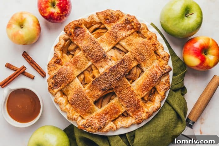 A whole caramel apple pie, baked to golden perfection with a decorative cheddar crust, rests in a pie dish on a green napkin, inviting a slice.