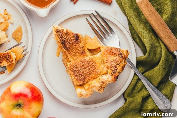 A single, inviting slice of apple pie rests perfectly on a white plate, showcasing its rich filling and golden crust.