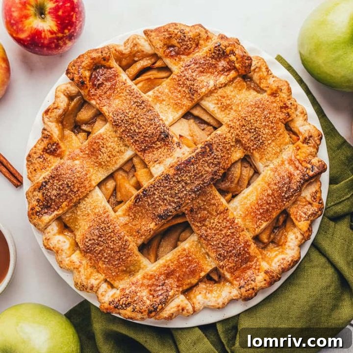 A freshly baked caramel apple pie with a golden cheddar crust, served in a pie dish on a green napkin, ready for slicing.