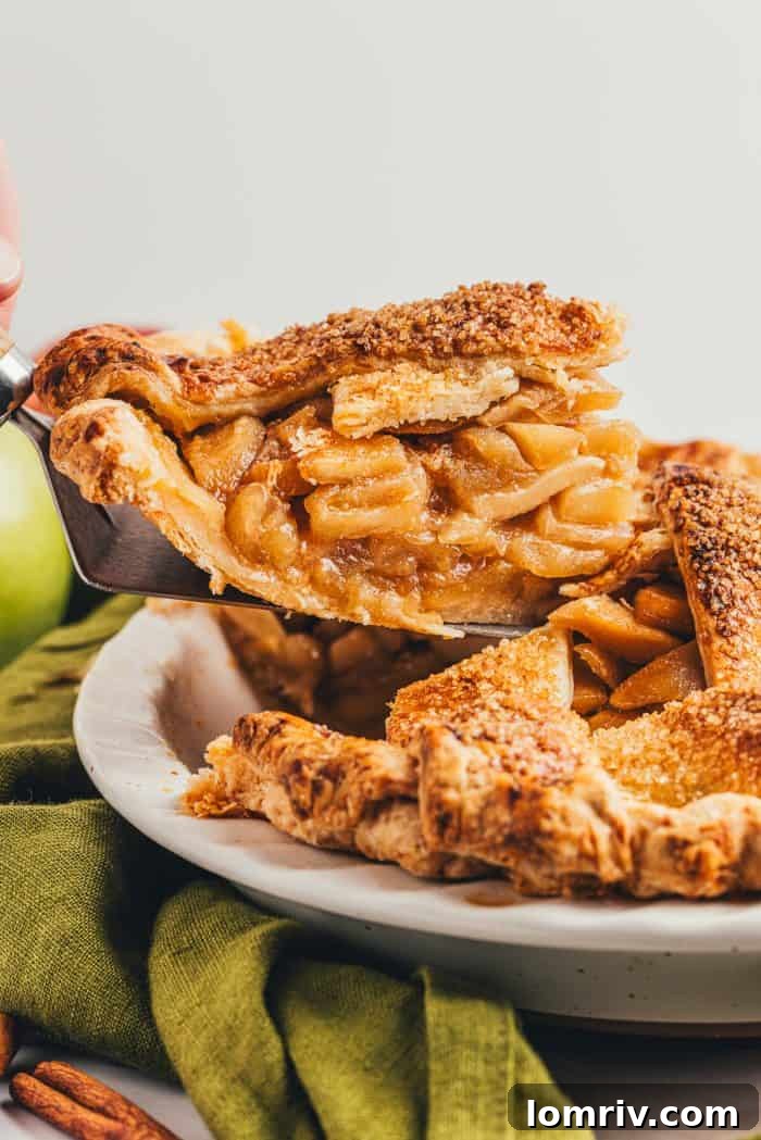 A perfect slice of warm caramel apple pie being carefully lifted from the whole pie, revealing its juicy apple layers.