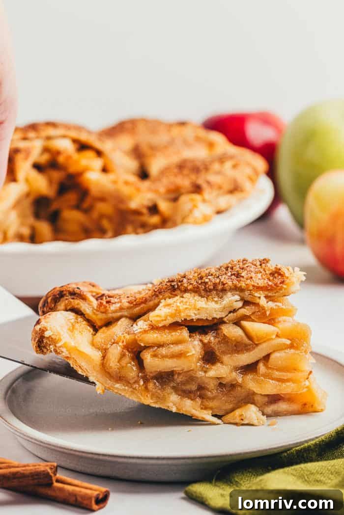 A freshly cut slice of homemade caramel apple pie is gently placed onto a pristine white plate, ready to be served.