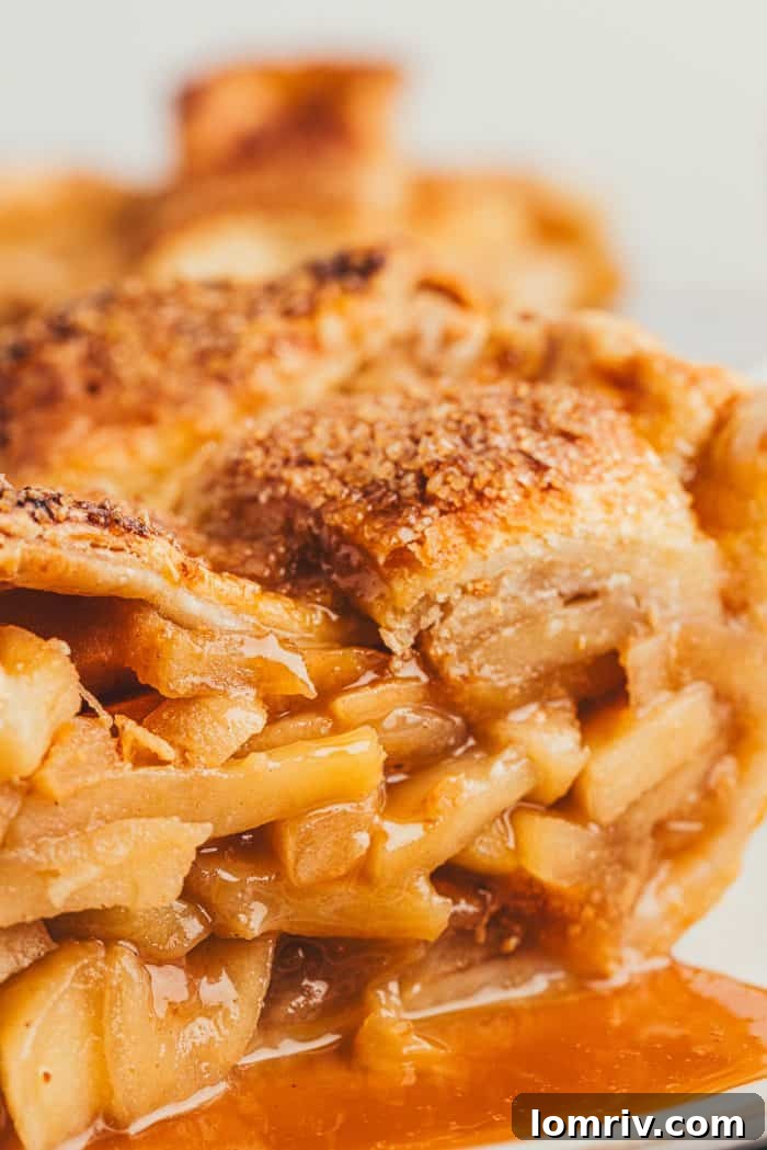 A close-up view of a slice of apple pie, revealing the perfectly cooked, layered apple slices and the luscious caramel sauce within.