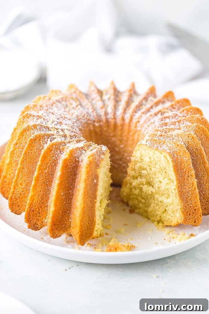 A perfect slice of Coconut Bundt Cake, showcasing its tender crumb and inviting texture, ready to be enjoyed. The cake is lightly dusted with powdered sugar.
