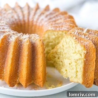 A beautifully decorated Coconut Bundt Cake, light golden brown, dusted with powdered sugar, and sitting on a white cake stand.