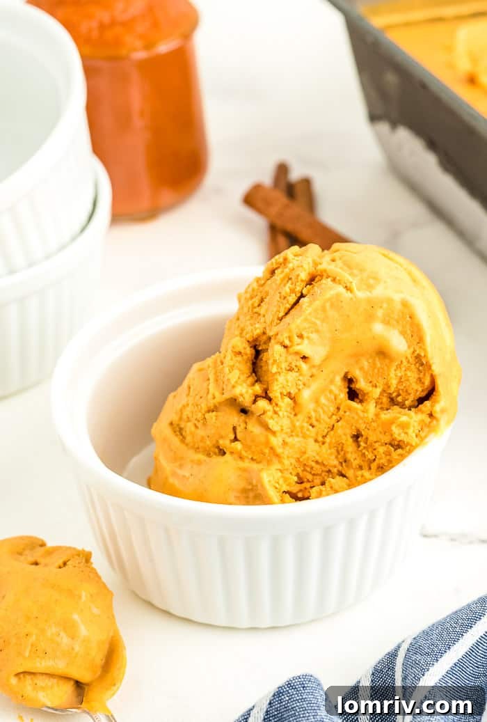 Several scoops of homemade Pumpkin Spice Cheesecake Ice Cream served in a clear bowl, highlighting its creamy texture and inviting appeal.