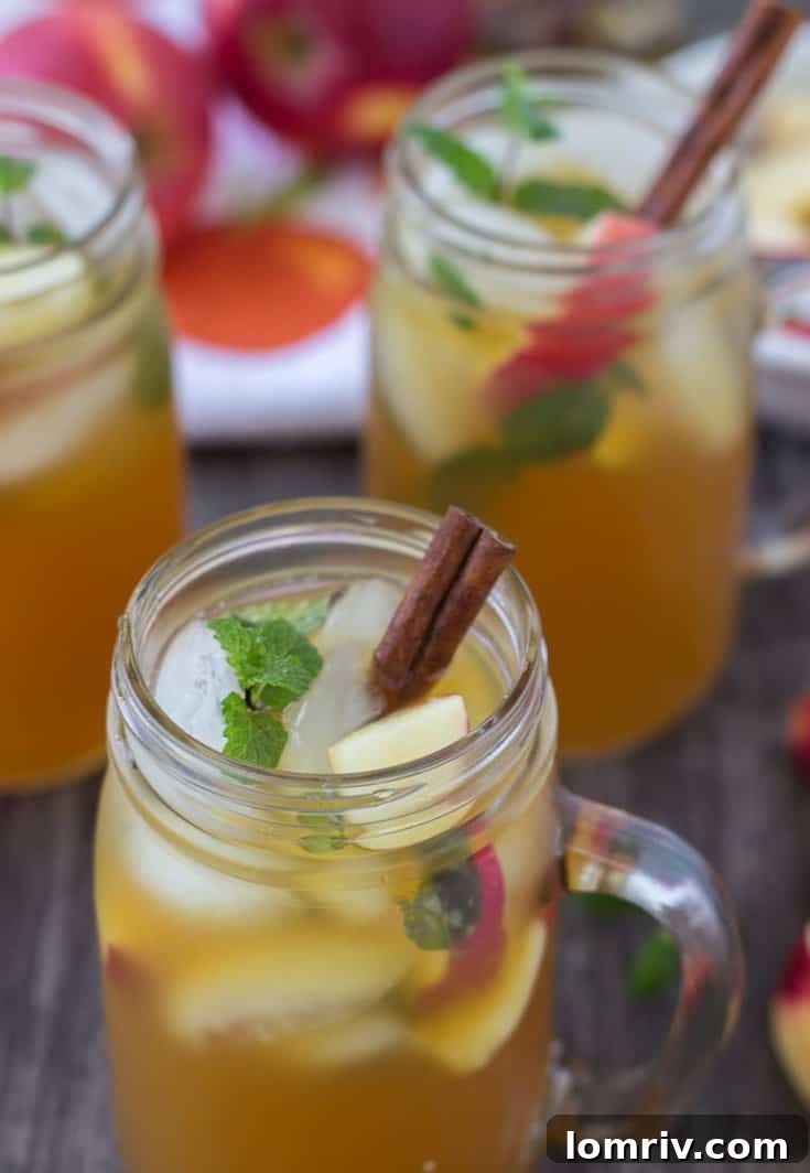A vibrant Apple Cider Mojito in a glass, garnished with cinnamon sticks and apple slices, set against an autumnal backdrop.