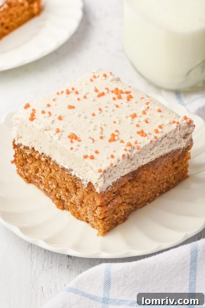 A closeup of a pumpkin cake bar, showing the moist cake and the creamy, speckled frosting.
