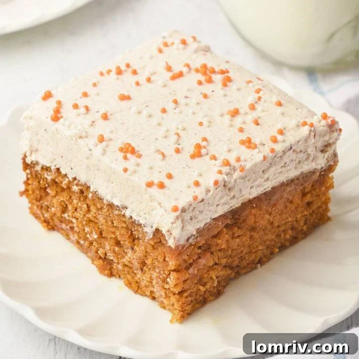 A closeup of a pumpkin cake bar, showing the moist cake and the creamy, speckled frosting.