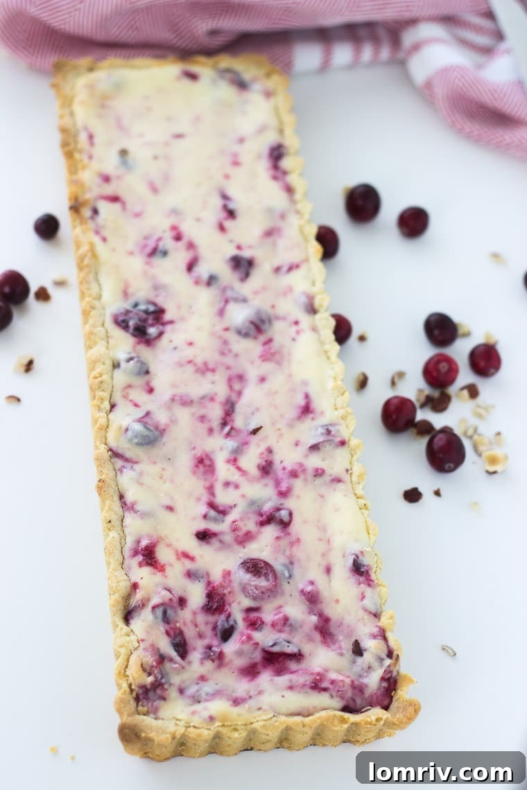 A beautifully presented cranberry hazelnut cream cheese tart with a slice removed, showing its creamy filling and nutty crust on a rustic wooden surface.