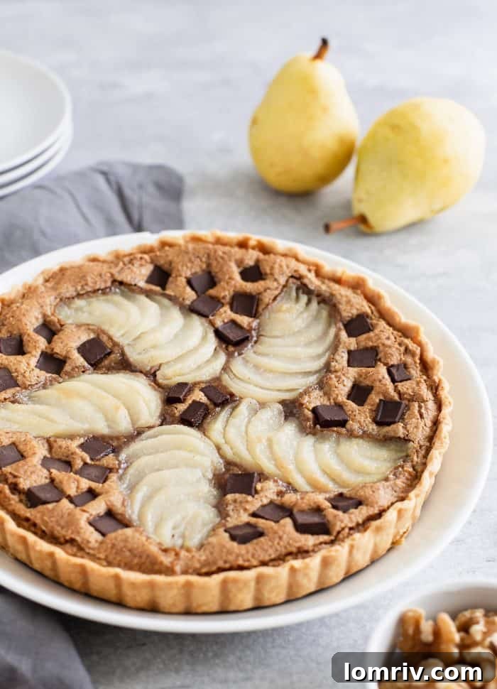A stunning hero shot of a freshly baked Pear Walnut Chocolate Tart, showcasing its golden, flaky crust and delicious filling with visible pears and melted chocolate chips. This visually appealing dessert is set to impress.