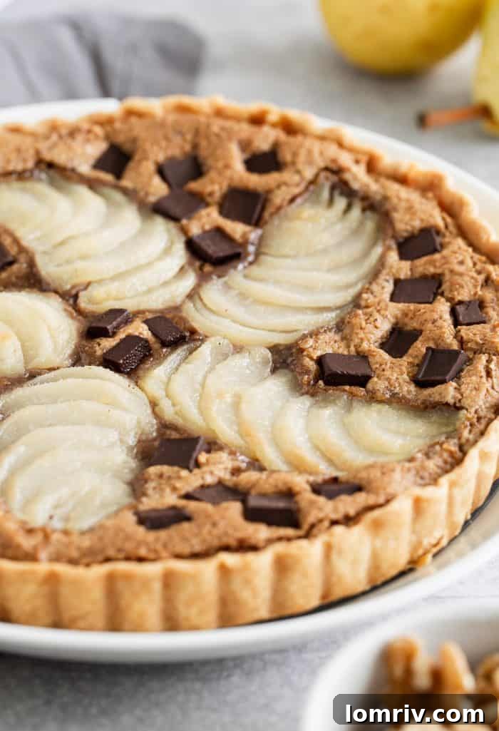 A close-up view of a slice of the Pear Walnut Chocolate Tart, revealing the tender poached pears, the rich walnut filling, and the glistening melted chocolate chips. This image emphasizes the tempting layers of this unique dessert.