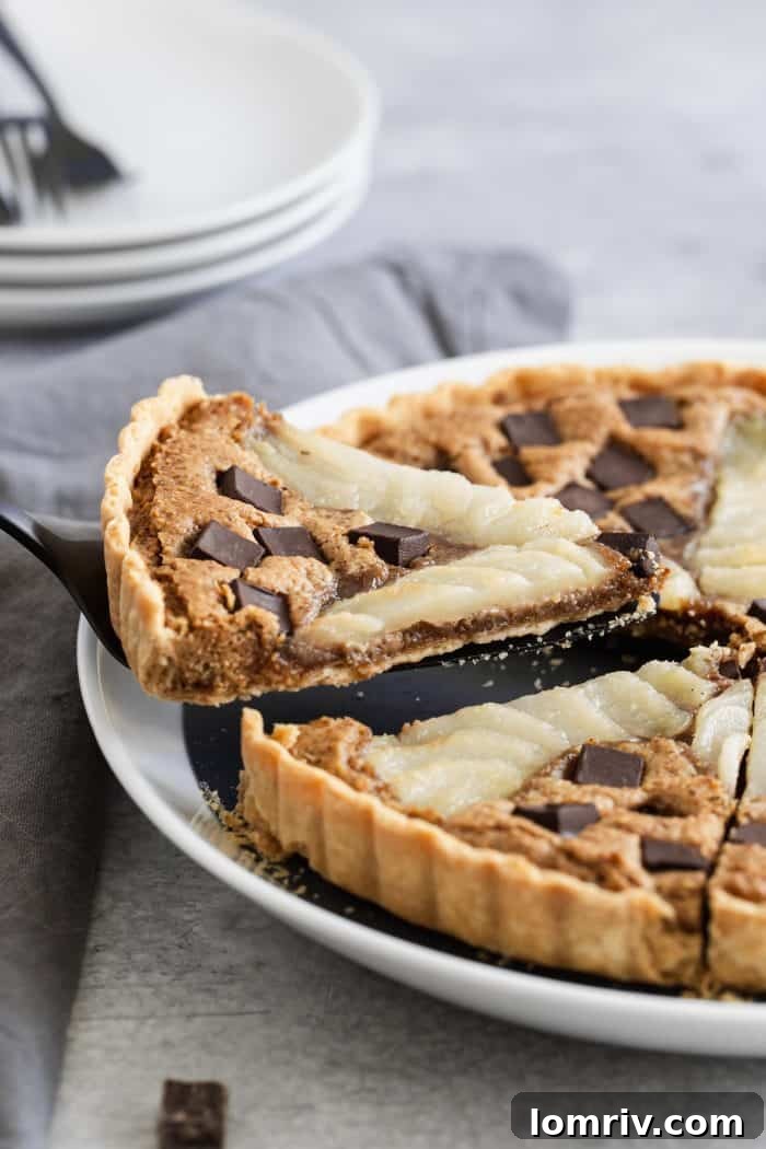 A close-up shot of a single slice of Pear Walnut Chocolate Tart, perfectly plated, showing the distinct layers of the golden crust, creamy walnut filling, and glistening chocolate alongside the soft pear. A truly inviting and gourmet dessert.