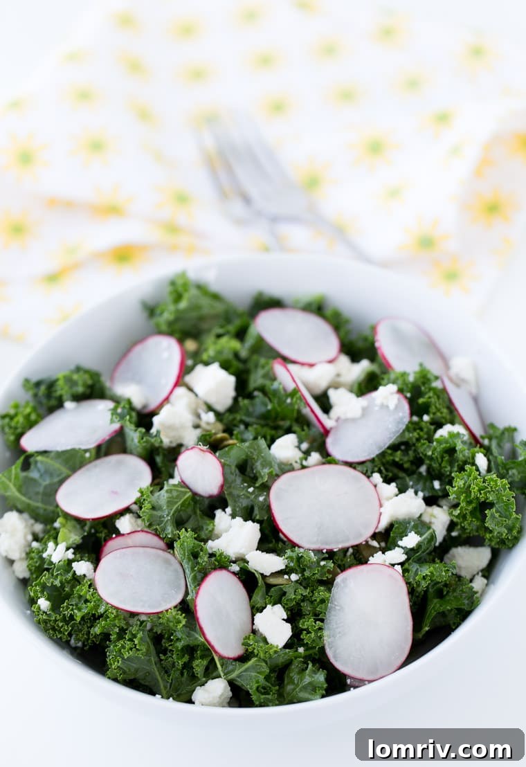 A close-up of a homemade kale salad bowl, showcasing the fresh kale, vibrant radishes, crunchy pepitas, and crumbled cojita cheese, ready to be dressed with lime vinaigrette.
