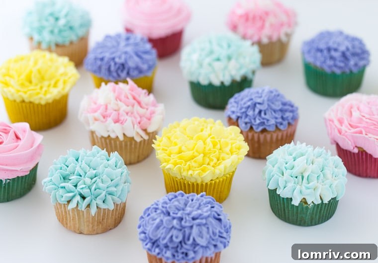 Essential ingredients and tools laid out on a table for making flower cupcakes, including piping bags, food coloring, and baked vanilla cupcakes.