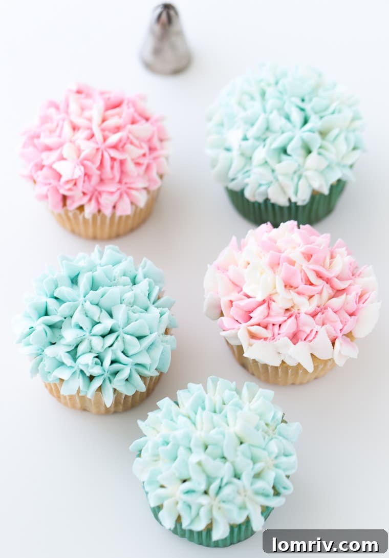 A collection of decorated flower cupcakes arranged on a white serving tray, highlighting the vibrant colors and detailed piping work.