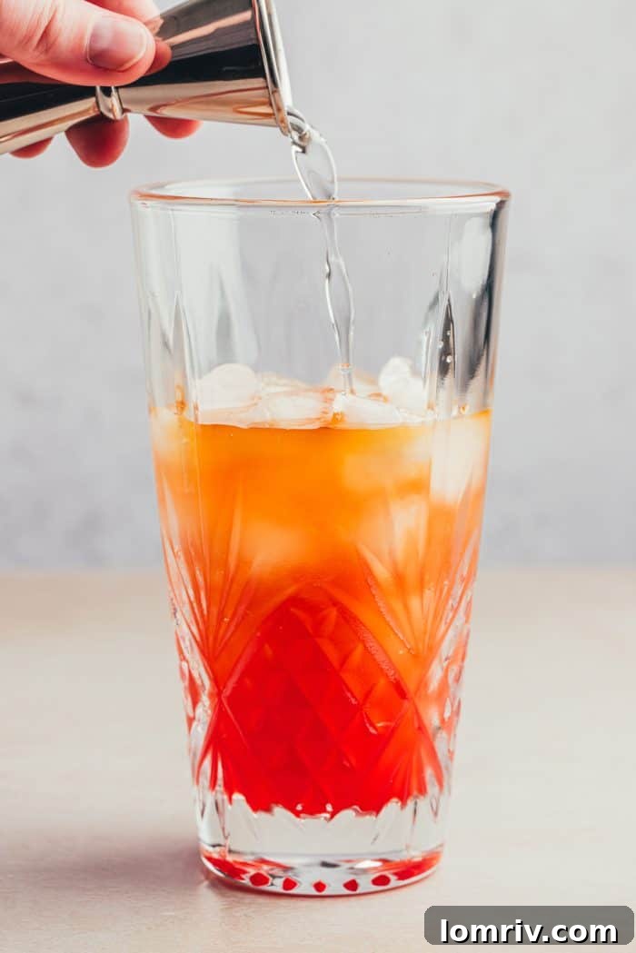 Simple syrup being poured into a glass with the ingredients for Planter's Punch.