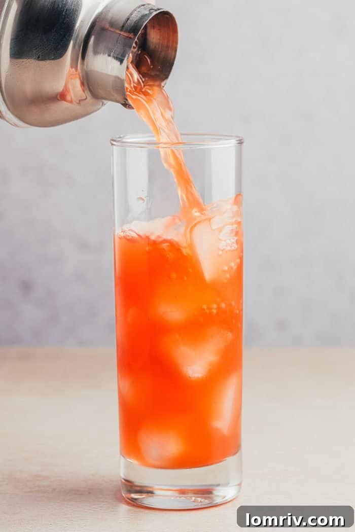 The cocktail being poured into a tall cocktail glass. 