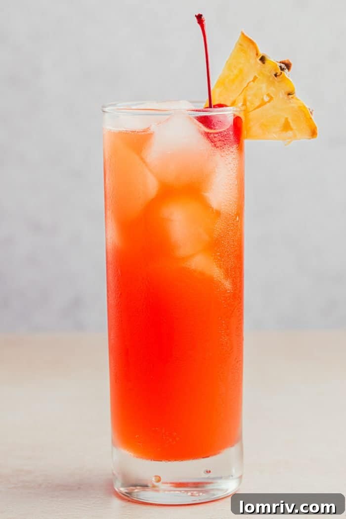 A glass filled with Planter's Punch and decorated with a maraschino cherry and a slice of pineapple.