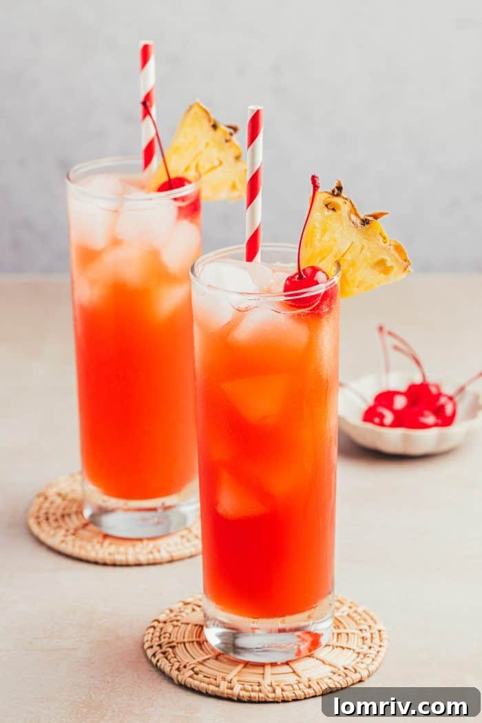 Two glasses filled with Planter's Punch and decorated with maraschino cherries and slices of pineapple.