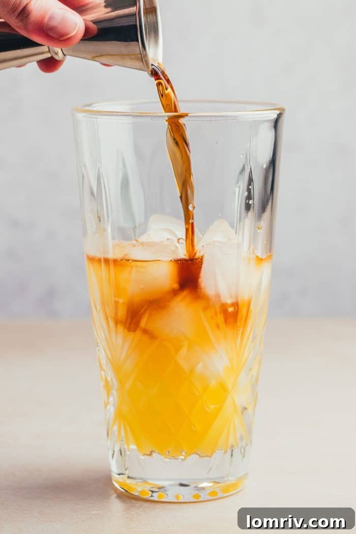 A glass filled with orange and pineapple juice with alcohol being poured into it.