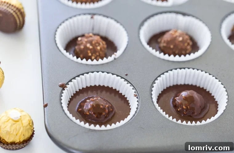 Cupcake batter covering the Ferrero Rocher for a hidden treat.