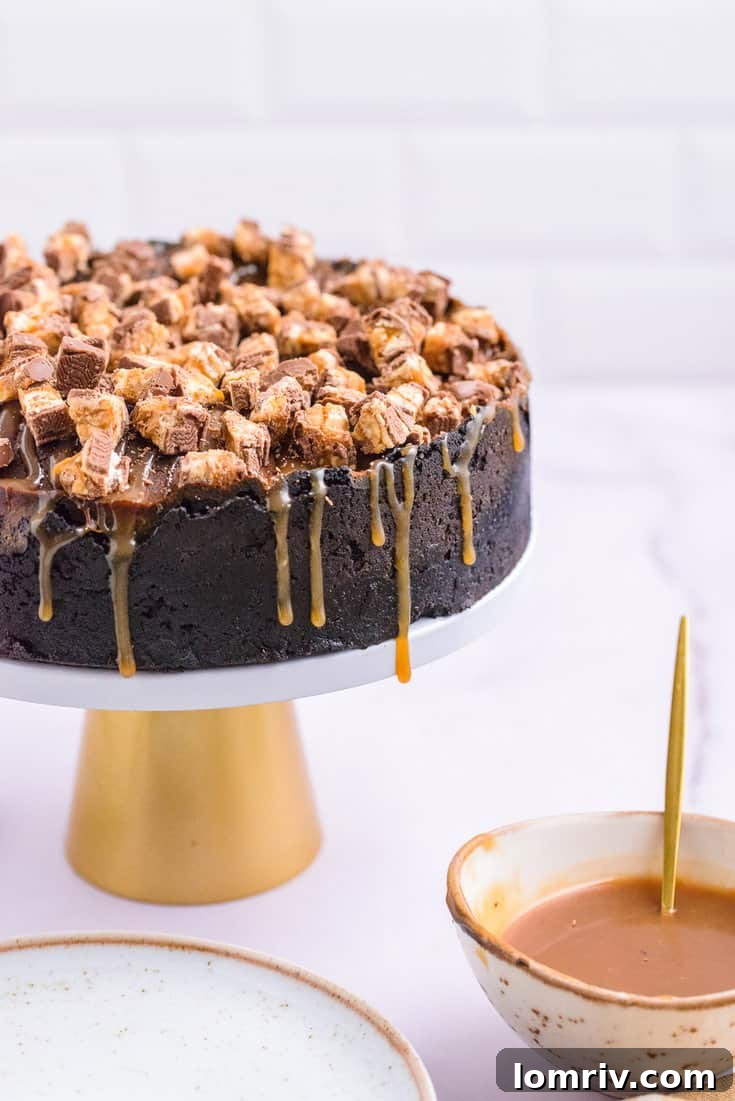 Decadent Snickers Peanut Butter Cheesecake with chocolate Oreo crust and salted caramel drizzle