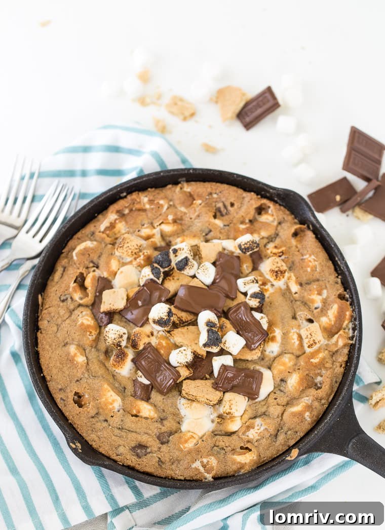 A slice of warm Skillet S'mores Cookie being scooped from the pan.