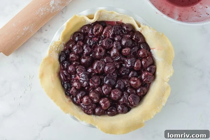 Cherry pie filling spooned into pie crust, ready for top crust
