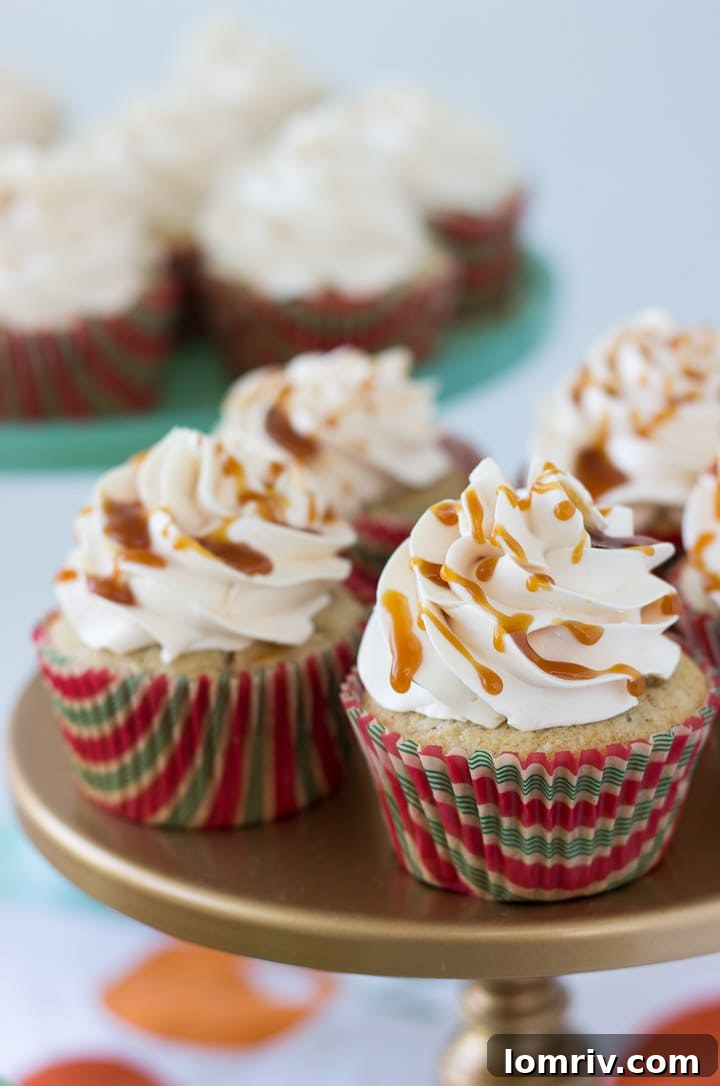 Close-up of three Salted Caramel Apple Cupcakes, topped with swirls of Swiss meringue buttercream and generous drizzles of golden salted caramel sauce, garnished with a tiny apple slice or cinnamon stick.