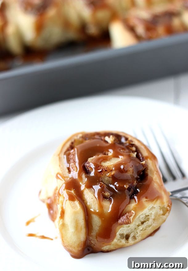 Warm Salted Caramel Apple Cinnamon Rolls, generously glazed with a sticky, golden salted caramel sauce and hints of baked apple visible within the swirls, presented on a rustic wooden board.