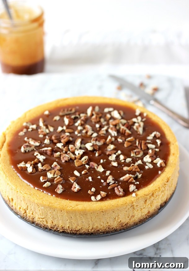 A slice of rich Pumpkin Pecan Cheesecake, topped with a generous drizzle of glossy salted caramel sauce and chopped pecans, sitting on a plate with a fork, ready to be enjoyed.