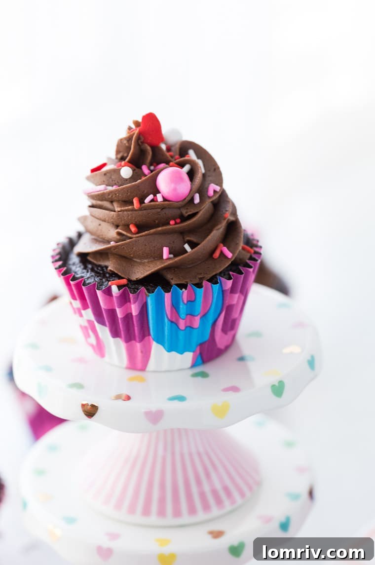 Three decadent chocolate cupcakes generously frosted with creamy chocolate buttercream and colorful sprinkles.