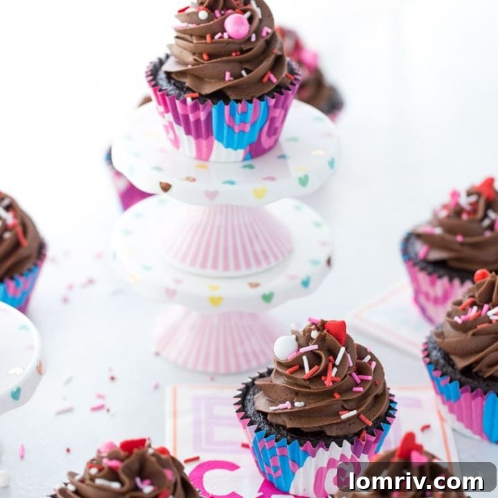 A plate of two irresistibly moist chocolate cupcakes, generously topped with a swirl of rich chocolate buttercream and decorative sprinkles.