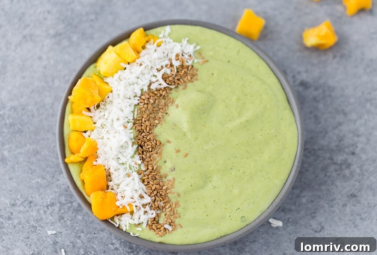 A close-up of a vibrant green mango coconut smoothie bowl with various healthy toppings.