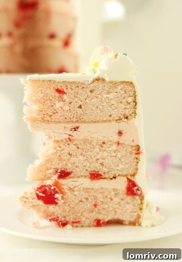 Close-up of a slice of Cherry Vanilla Champagne Cake, showing the moist layers, cherry filling, and fluffy buttercream. Get the recipe on AClassicTwist.com