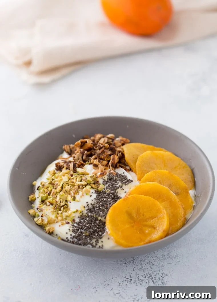 A close-up view of the ingredients in the roasted persimmon yogurt bowl, meticulously arranged to show creamy Greek yogurt, golden roasted persimmon slices, crunchy granola, vibrant green pistachios, and chia seeds, all drizzled with honey.