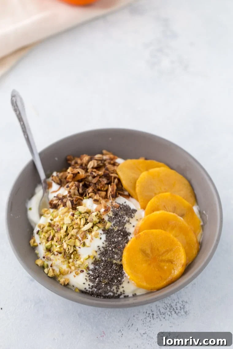 A close-up shot of a spoon scooping into the roasted persimmon yogurt bowl, revealing the layers of creamy yogurt, tender persimmons, and crunchy toppings, ready to be eaten.