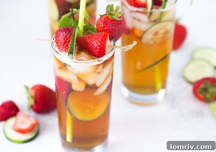 A close-up of the Classic Pimm's Cup in a glass, with ice, strawberries, cucumber, and mint, highlighting its refreshing quality.