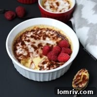 Garnished Vanilla Bean Crème Brûlée with fresh raspberries, showcasing a ready-to-eat dessert