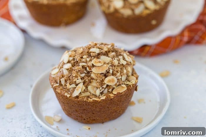 Close-up of a moist, hearty pumpkin spice carrot muffin with visible walnuts and a streusel topping, perfect for fall mornings.